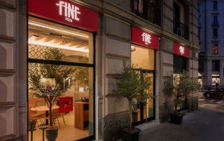 L'esterno del locale pizza Fine Milano. Dalle vetrate illuminate si vedono gli interni dai colori caldi del legno.