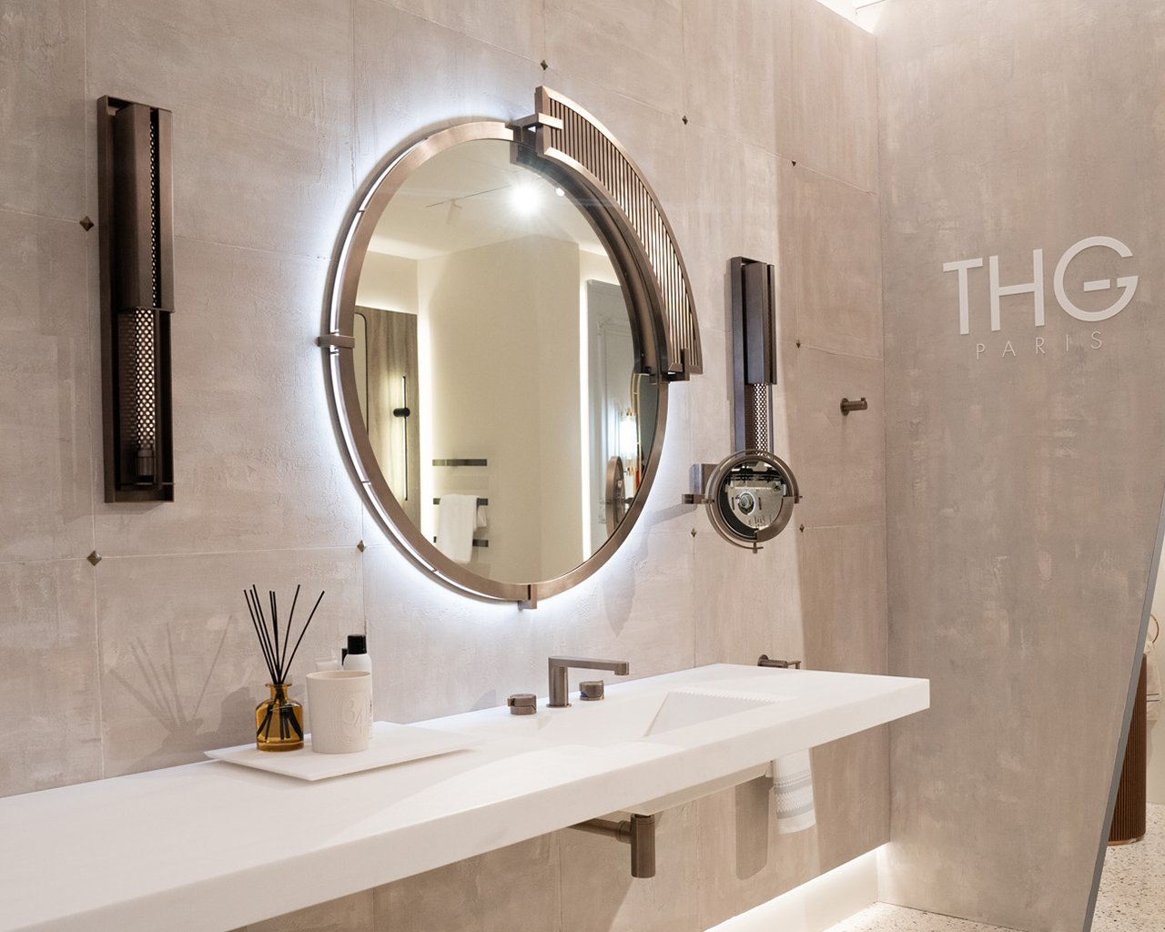 Uno specchio tondo svetta su una parete lucida e bianca con eleganti mobili da bagno bianchi.