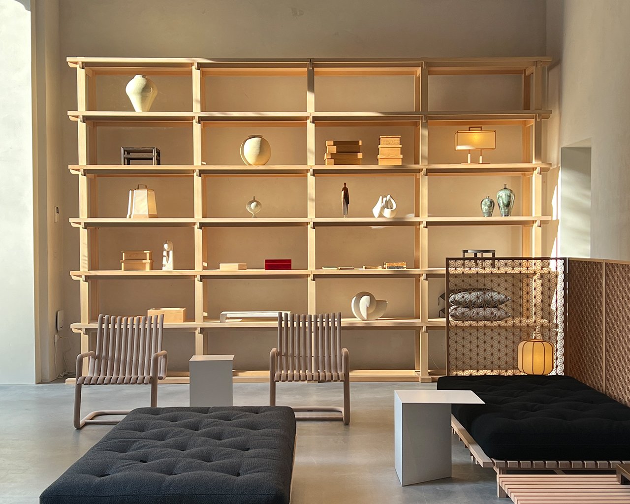 Un dettaglio degli spazi interni, una libreria in legno naturale con oggetti esposti, e a terra degli eleganti futon e altri complementi d'arredo.